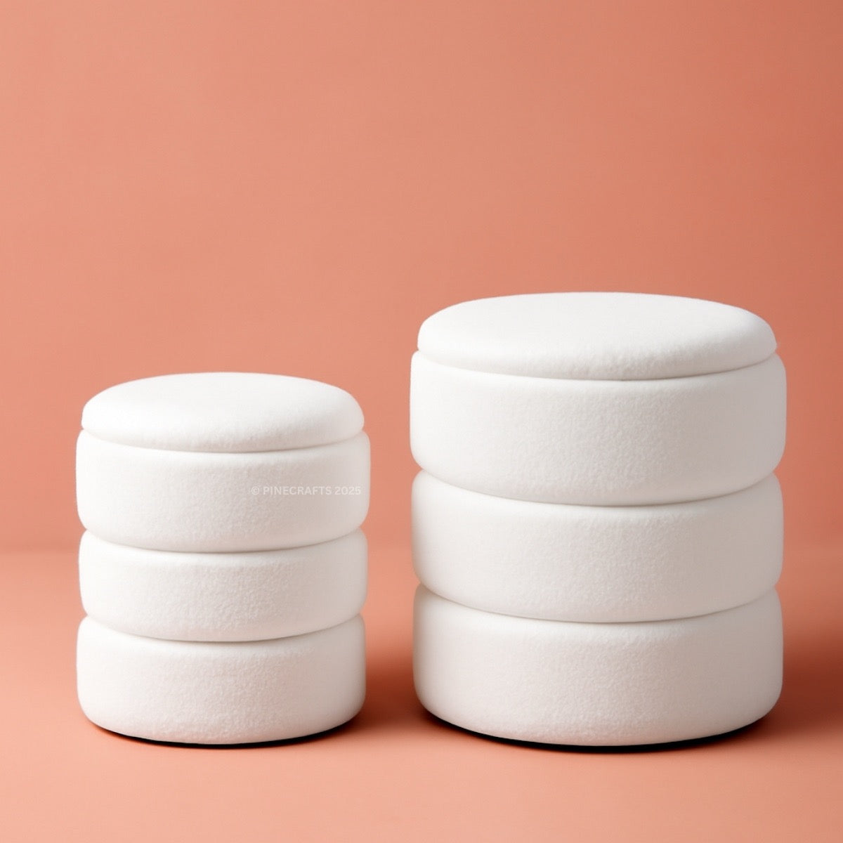 Two white cylindrical stools stacked on a peach background